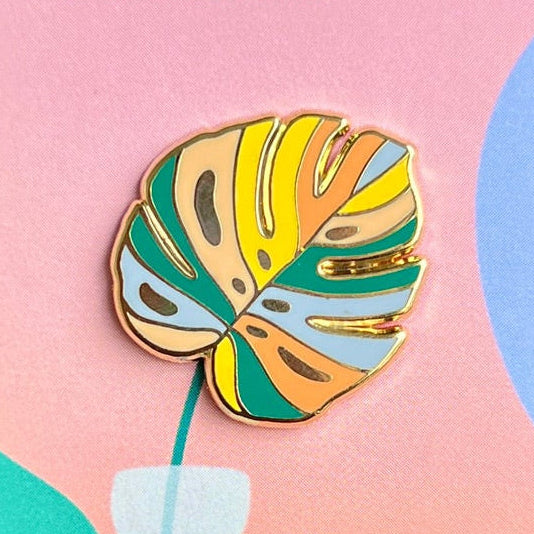 Enamel pin packaging with a pineapple design held against a green leafy background